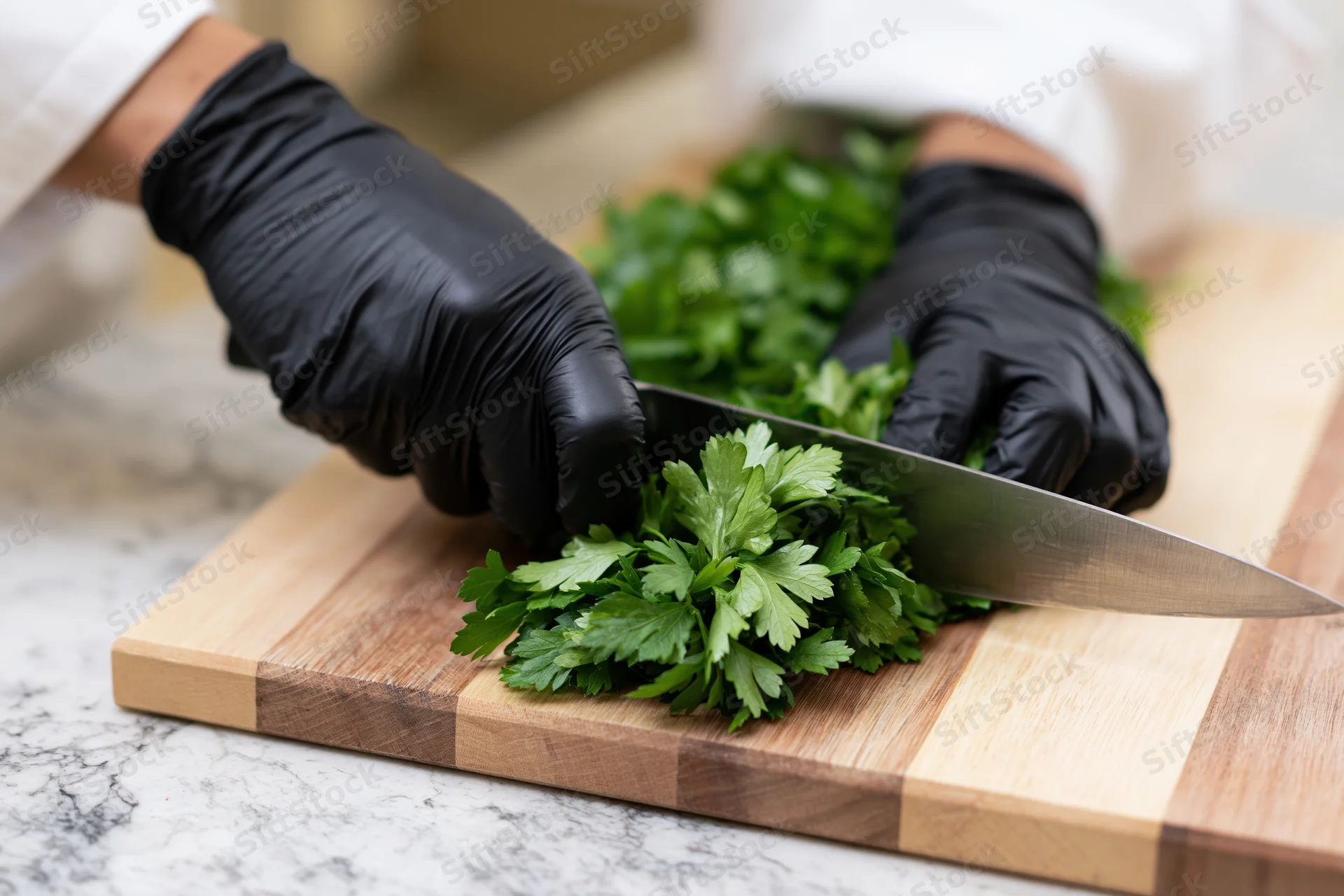 Chef's hands in black nitrile gloves chopping fresh parsley on a wooden cutting board