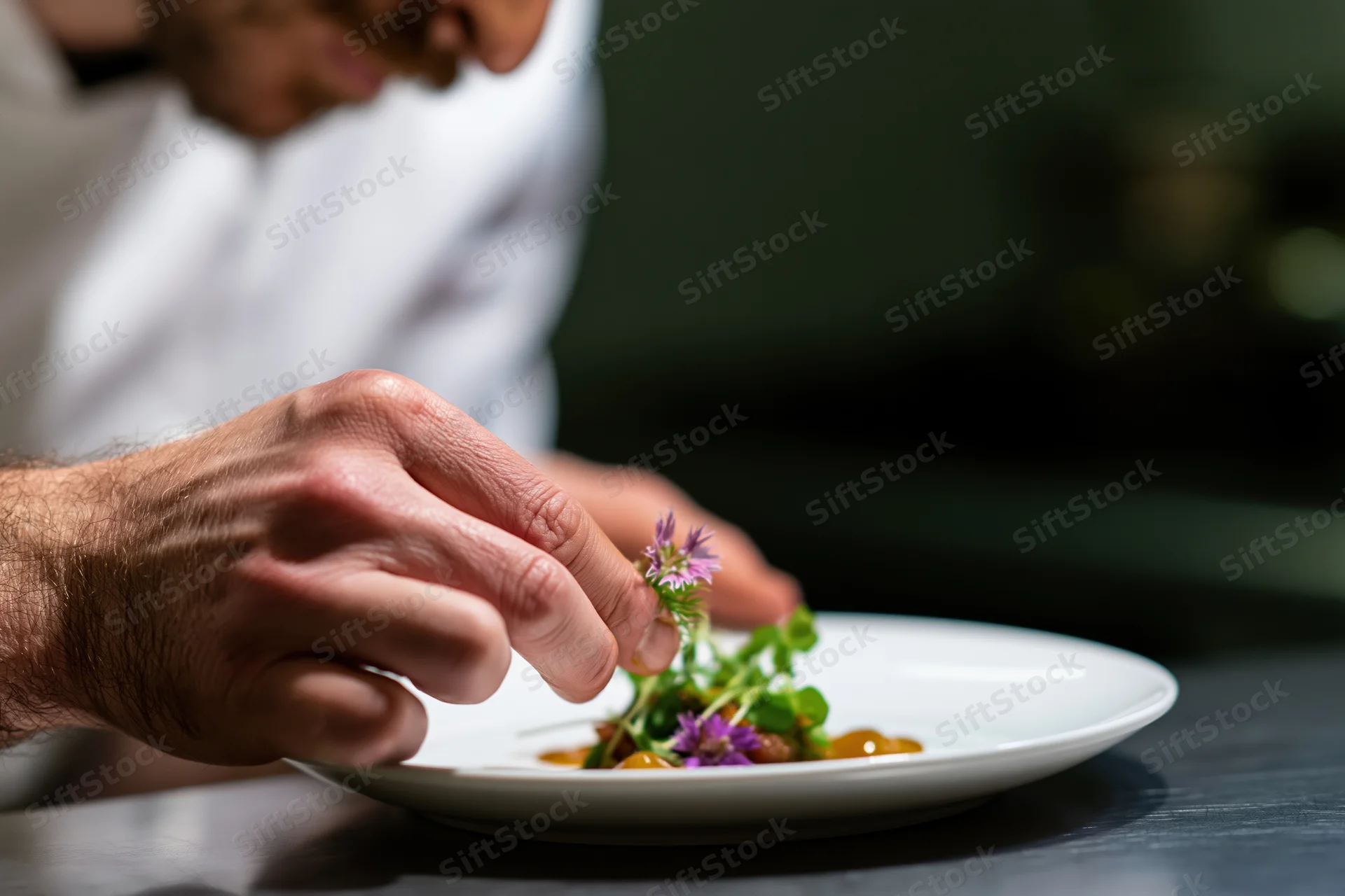Chef placing edible flower on plated dish in fine dining kitchen