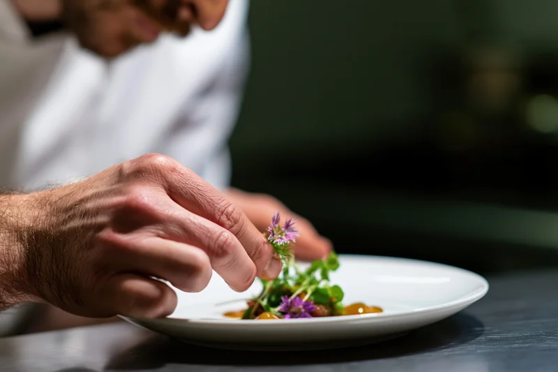 Chef placing edible flower on plated dish in fine dining kitchen
