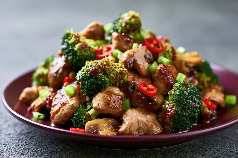 Stir-fried chicken and broccoli with mushrooms and red chili slices on a dark plate