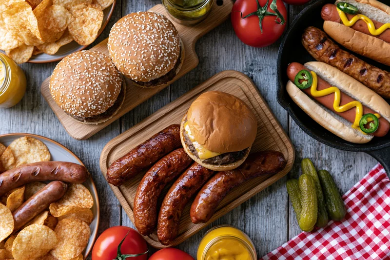 Overhead view of a classic american barbecue spread with burgers, sausages, hotdogs, chips, and condiments on a weathered wooden table