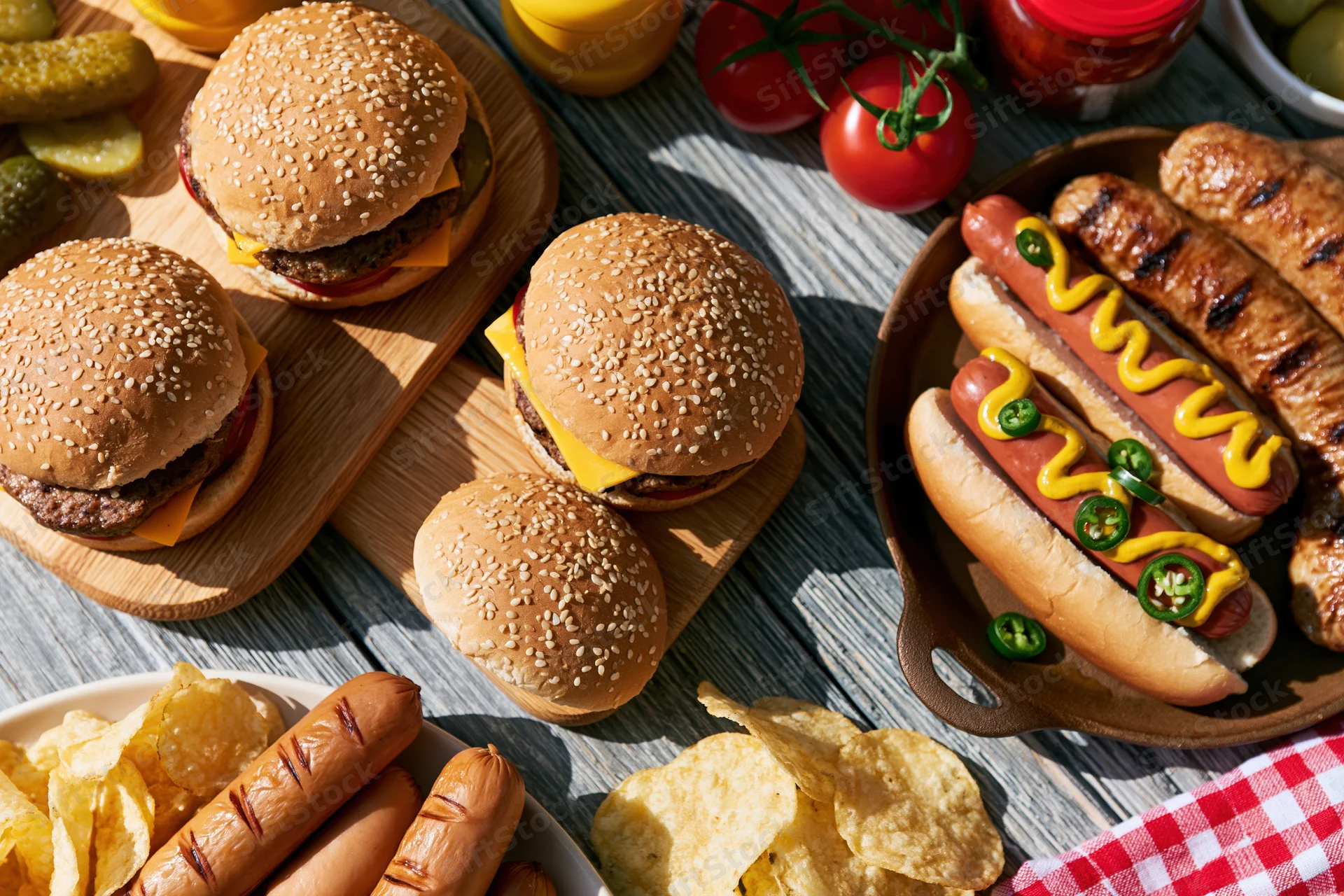 Grilled burgers and hotdogs with condiments and sides on a weathered wooden table