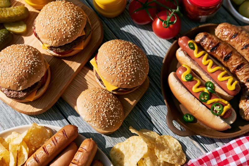 Grilled burgers and hotdogs with condiments and sides on a weathered wooden table