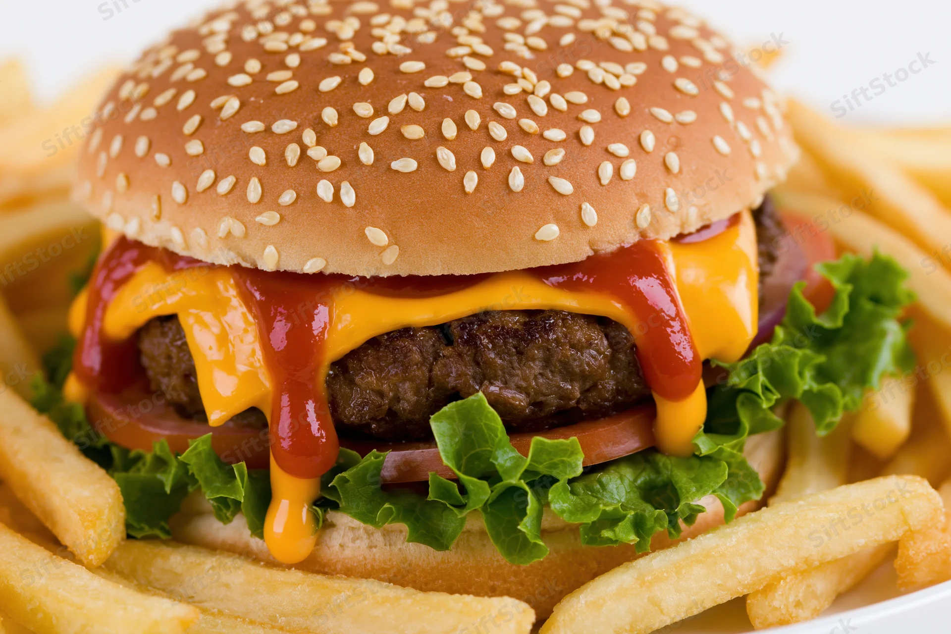 Cheeseburger with sesame seed bun, beef patty, melted cheese, ketchup, lettuce, tomato, and onion, served with french fries on a white plate