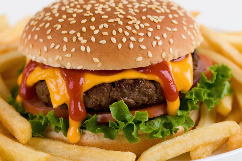 Cheeseburger with sesame seed bun, beef patty, melted cheese, ketchup, lettuce, tomato, and onion, served with french fries on a white plate