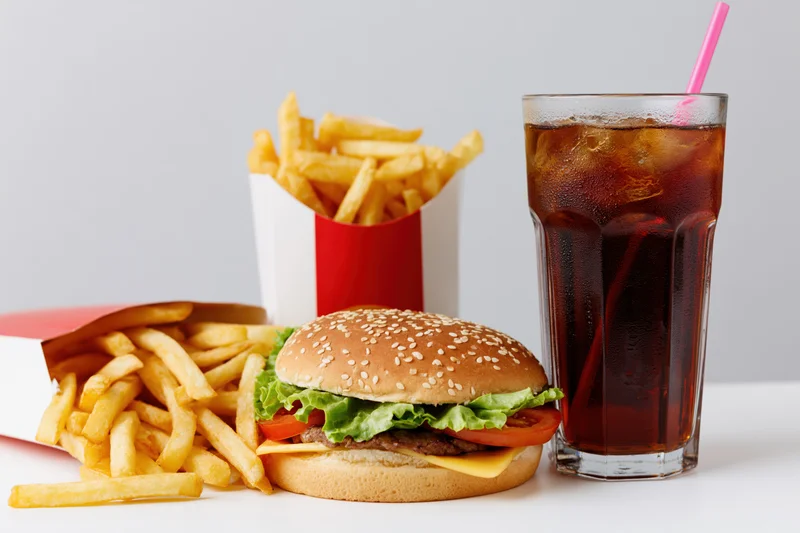 Hamburger with french fries and soda arranged on a white surface