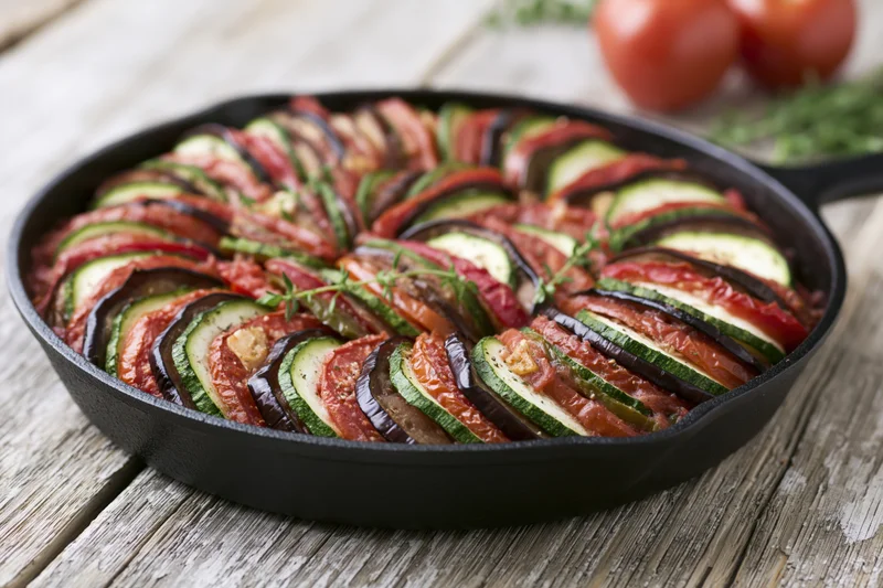 Ratatouille arranged in concentric layers in a cast iron skillet on a wooden table