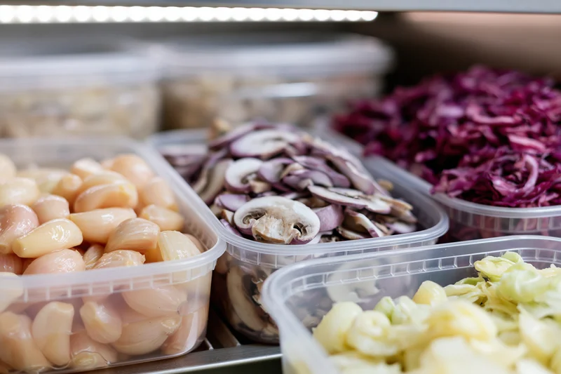 Clear plastic deli containers filled with prepped vegetables on a refrigerated shelf