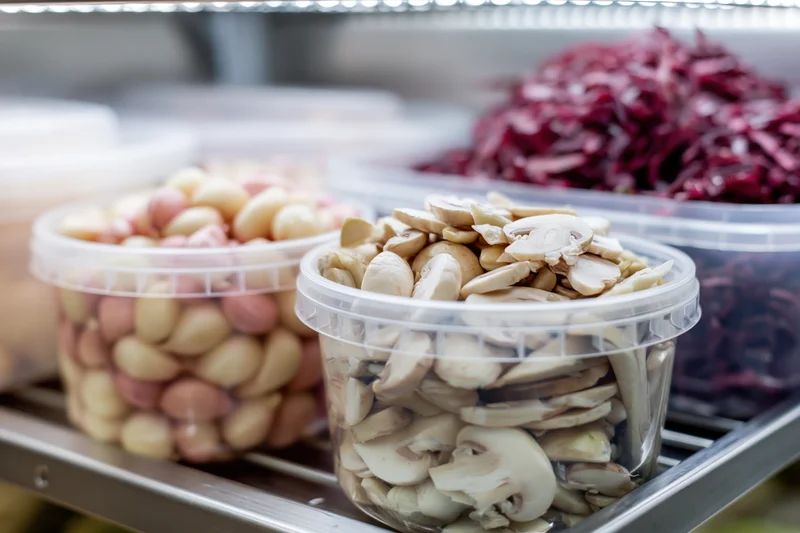 Sliced mushrooms and garlic in clear plastic deli containers on a refrigerated shelf
