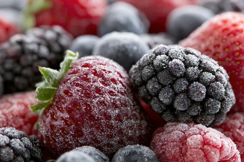 Close-up of mixed frozen berries including strawberries, blackberries, raspberries and blueberries with frost on their surfaces