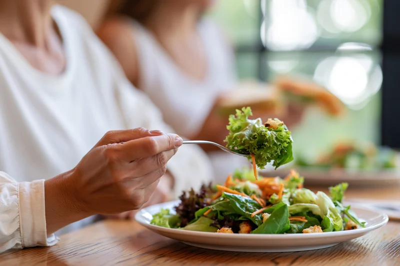 Woman lifting a forkful of fresh green salad at a wooden dining table in a restaurant