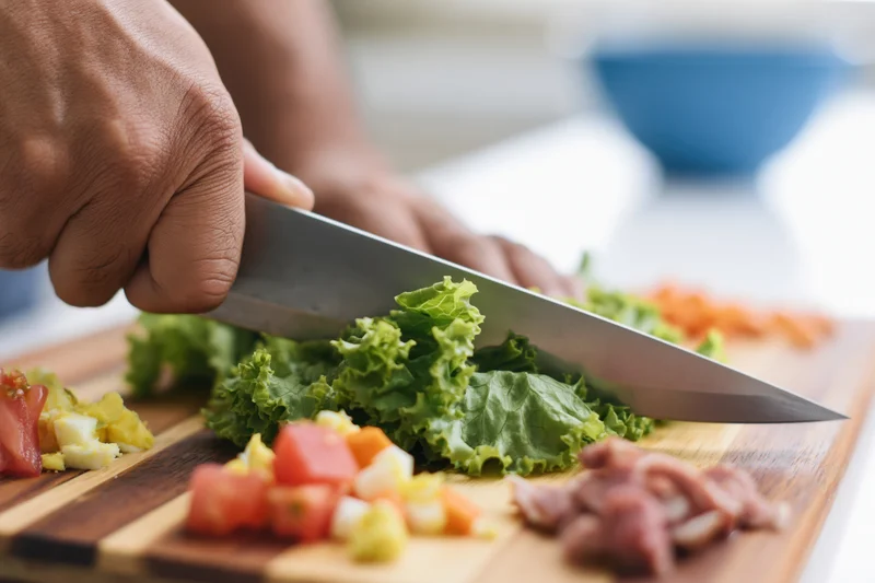 Hand chopping salad ingredients on a wooden cutting board in a kitchen