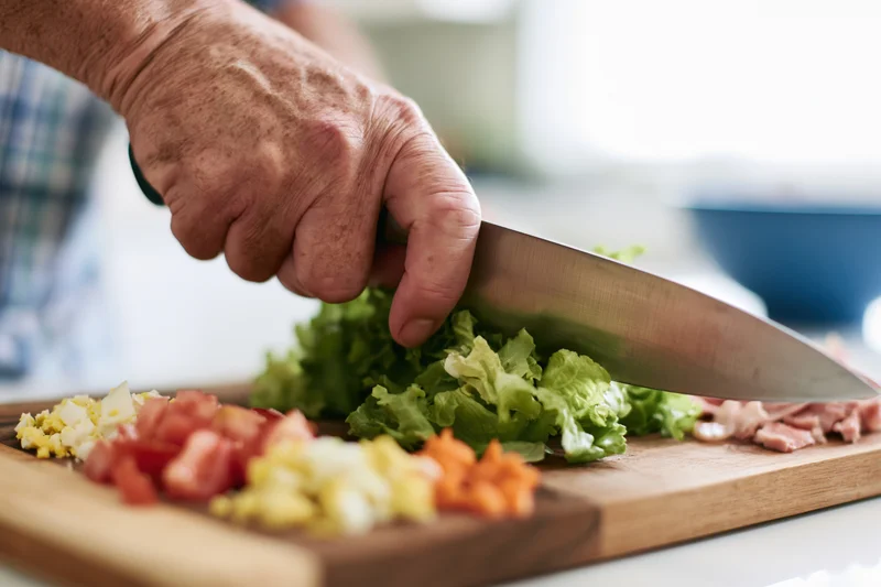 Hand chopping lettuce and vegetables on a wooden cutting board in a kitchen