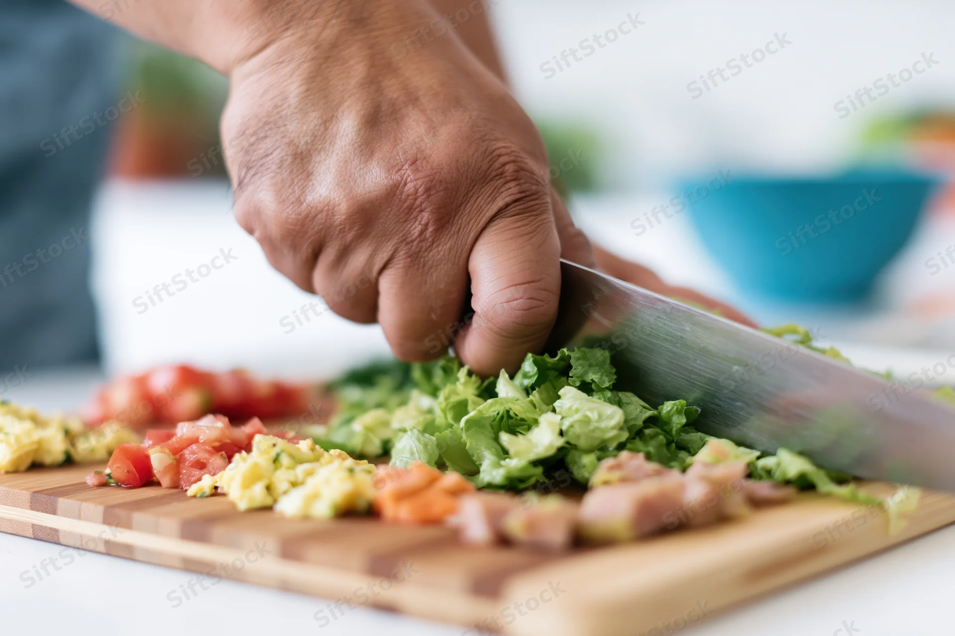 Hand chopping vegetables and meat on a bamboo cutting board in a kitchen