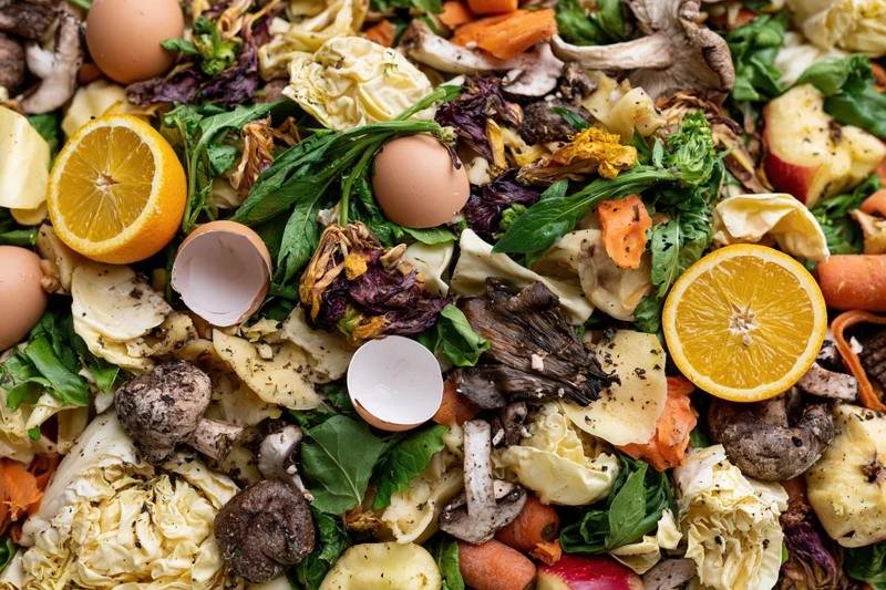 Close-up overhead view of mixed food scraps including fruit peels, vegetable trimmings, eggshells and wilted greens piled together