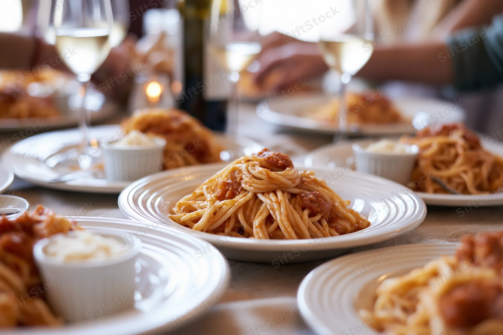 Plates of spaghetti with meatballs and wine glasses on a dinner table during a social gathering