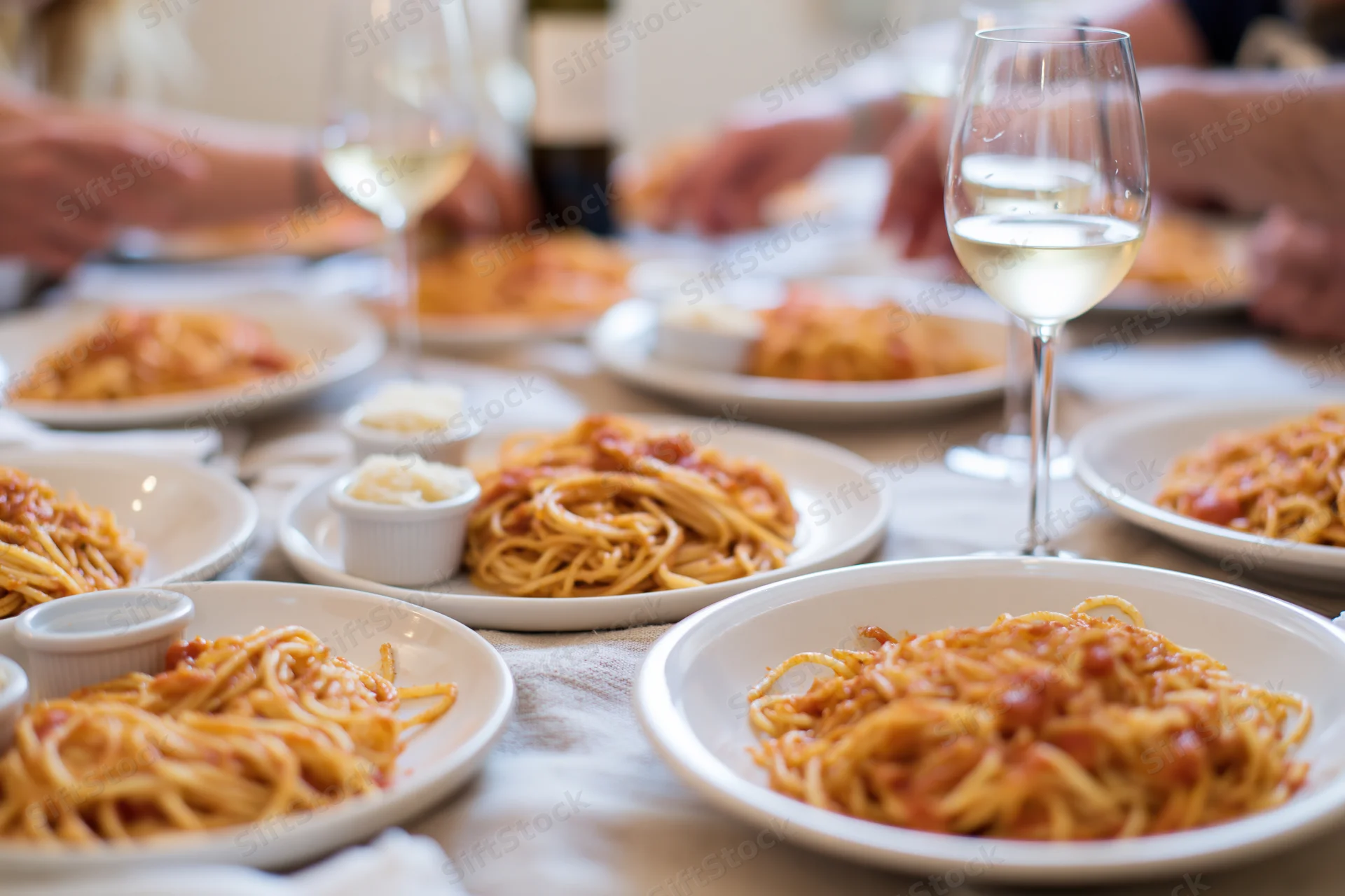Plates of spaghetti with tomato sauce and wine glasses on a dinner table with hands serving food