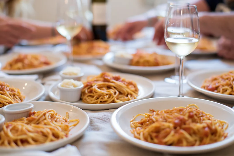 Plates of spaghetti with tomato sauce and wine glasses on a dinner table with hands serving food