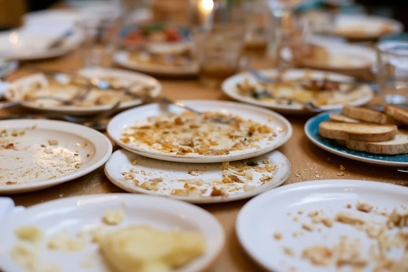 Cluttered dining table with empty plates and crumbs after a shared meal in a restaurant