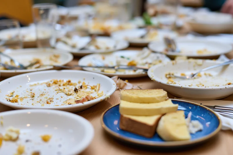 Cluttered dining table with empty plates and crumbs after a shared meal