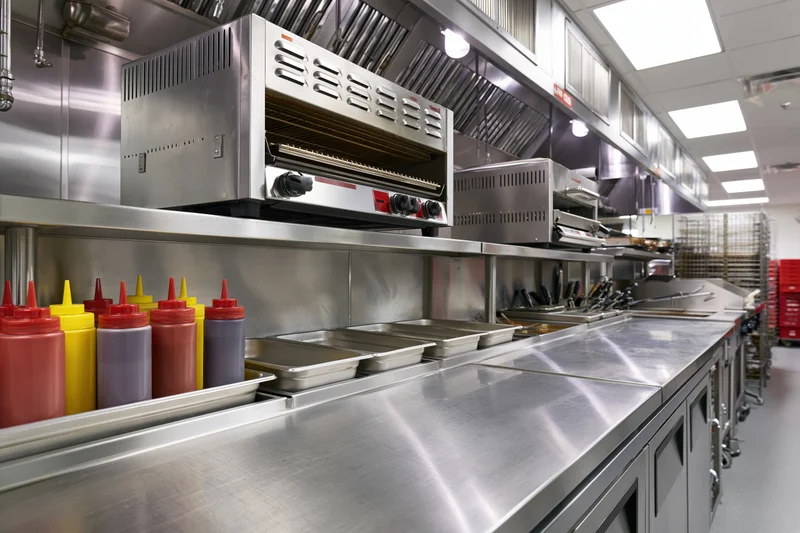 Stainless steel commercial kitchen prep line with condiment bottles and cooking equipment ready for service
