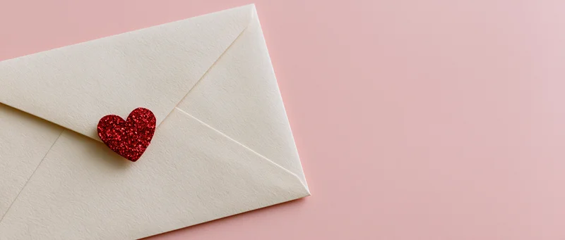Cream envelope with red glitter heart on pink surface