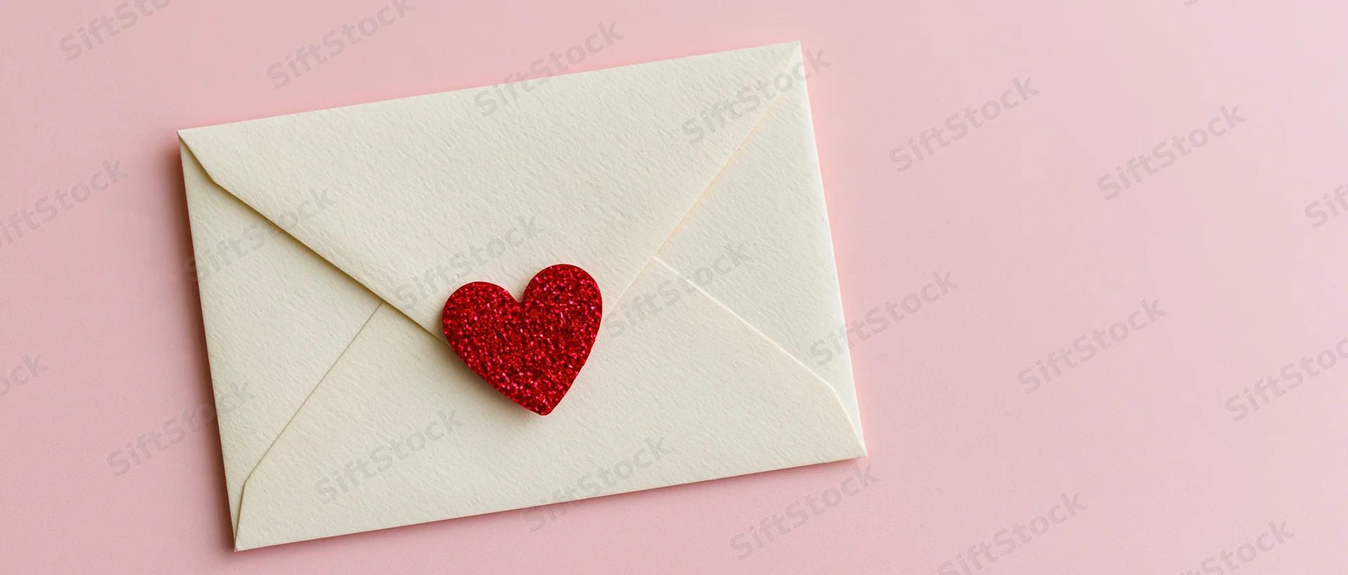 Cream envelope with red glitter heart on pink surface