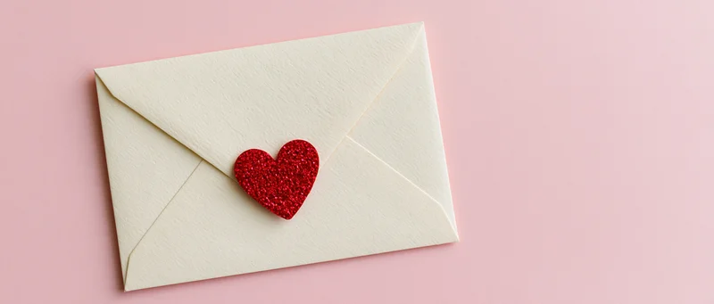 Cream envelope with red glitter heart on pink surface