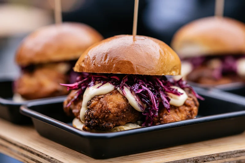 Crispy fried chicken sandwich in a glossy brioche bun with purple cabbage and sauce on a black tray