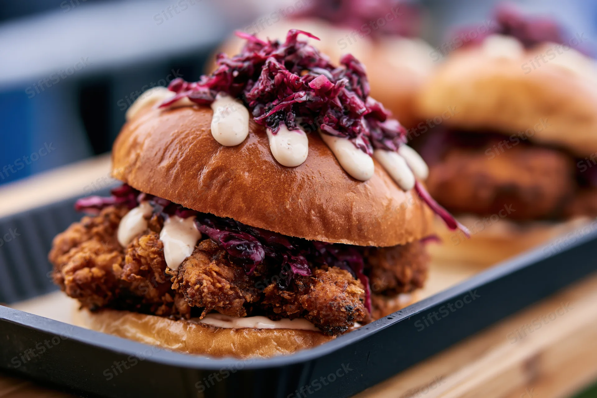 Crispy fried chicken sandwich in a glossy brioche bun with red cabbage slaw and sauce on a black tray
