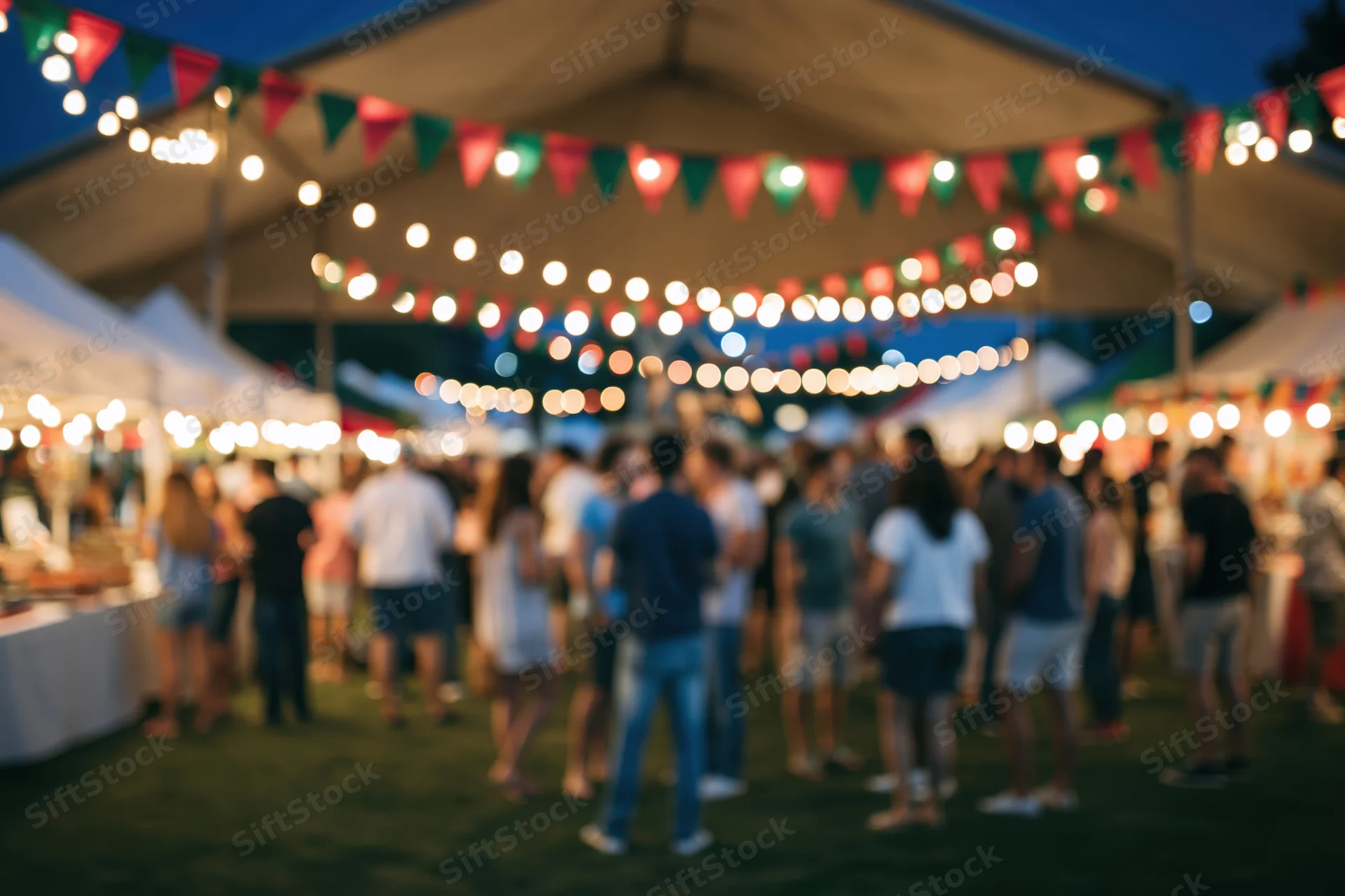 Crowd of people milling around an outdoor night market under string lights and tents