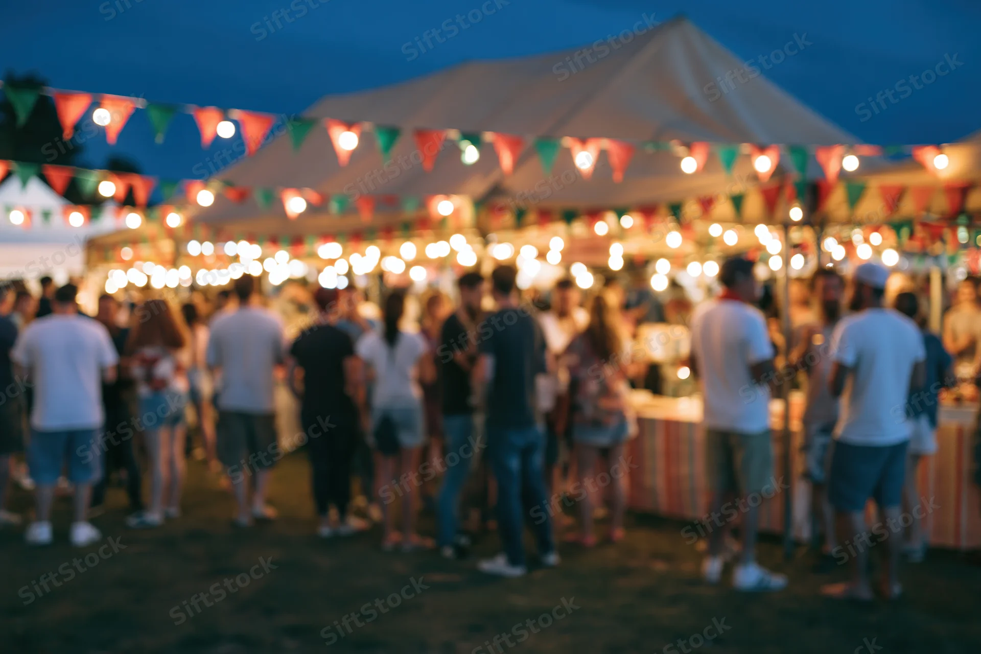 Crowd of people milling around an outdoor night market under illuminated tents and string lights