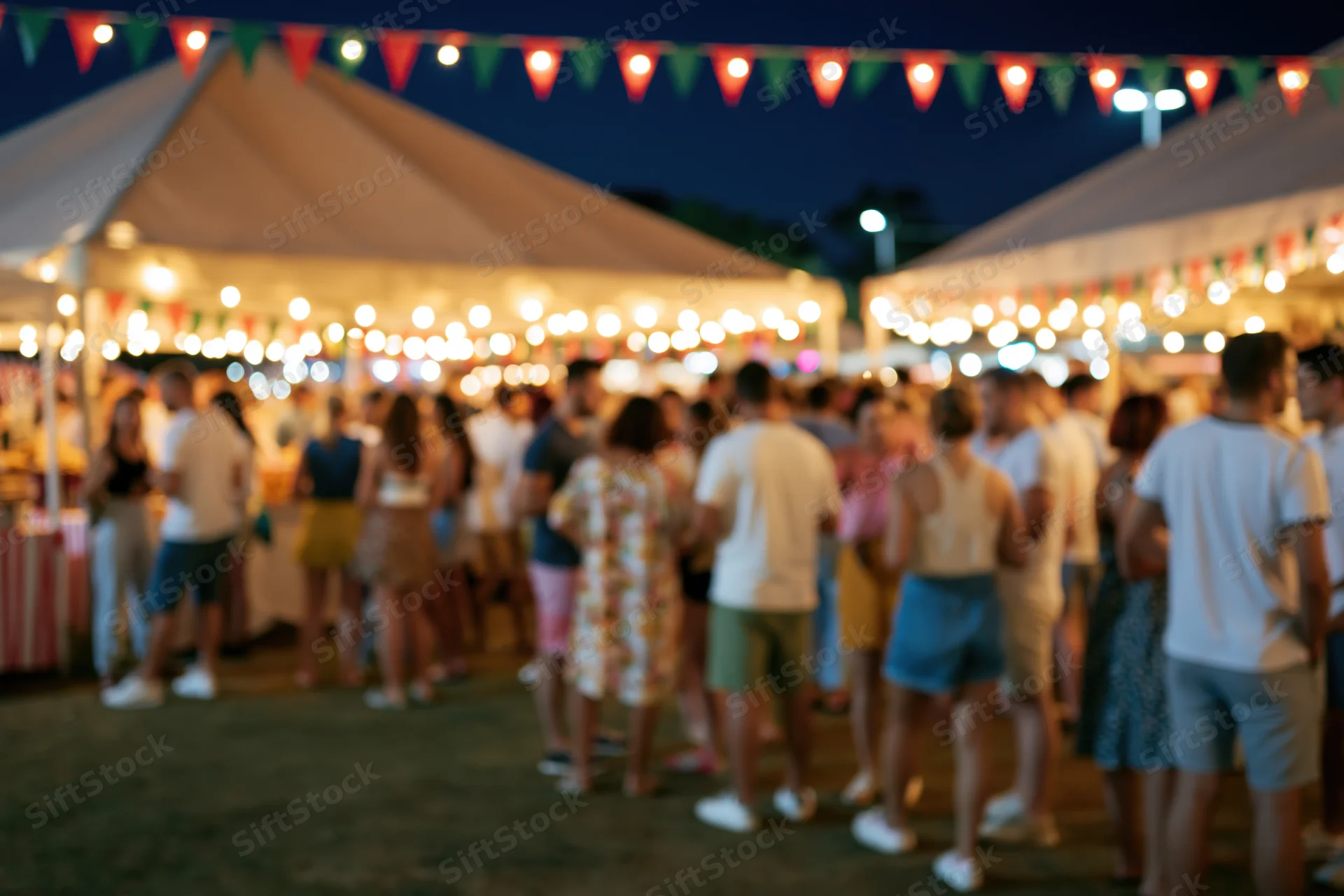 Crowd of people milling around an outdoor night market under string lights and tents at evening