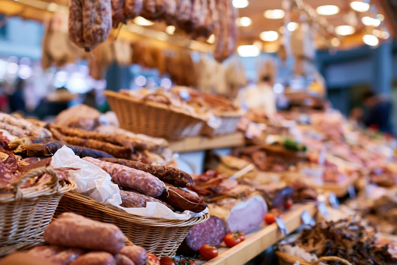 Cured meats displayed in baskets and on shelves at a European market stall