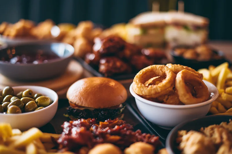 Burger on a crowded restaurant table with various side dishes and snacks arranged around it