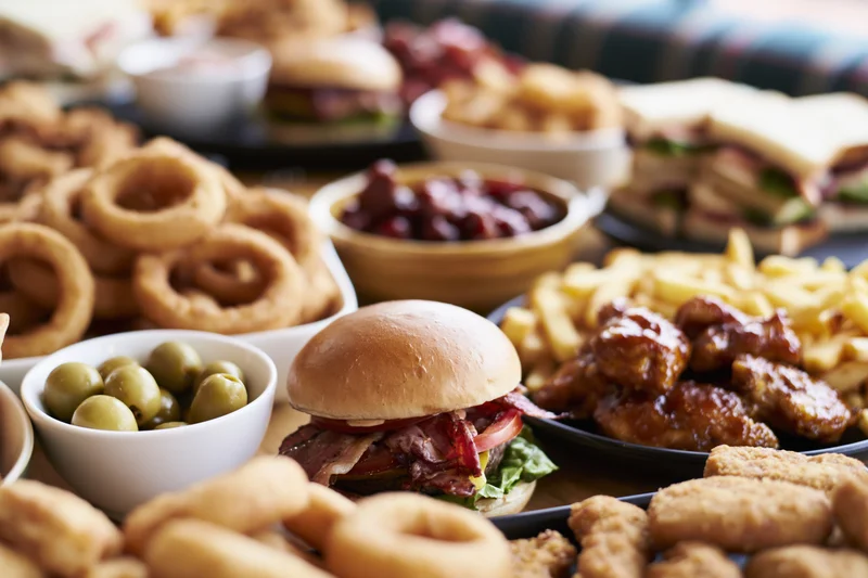 Burger on a crowded restaurant table surrounded by fries, onion rings, chicken wings, and side dishes