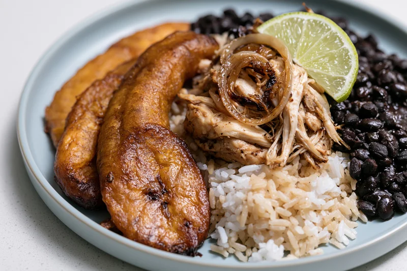 Cuban plate with fried sweet plantains, white rice, black beans, and shredded chicken topped with caramelized onions and lime slice