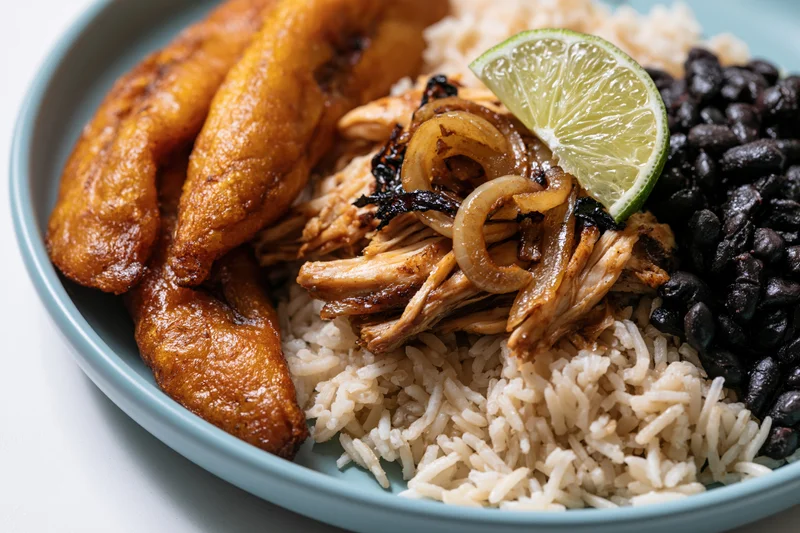 Cuban plate with fried sweet plantains, white rice, black beans, and shredded chicken topped with lime and onions