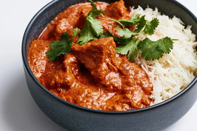 Butter chicken curry with rice and cilantro garnish in a dark matte ceramic bowl