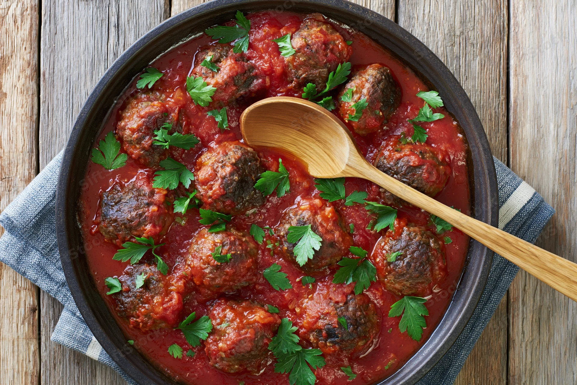 Meatballs in tomato sauce with parsley garnish in a dark skillet on a wooden table