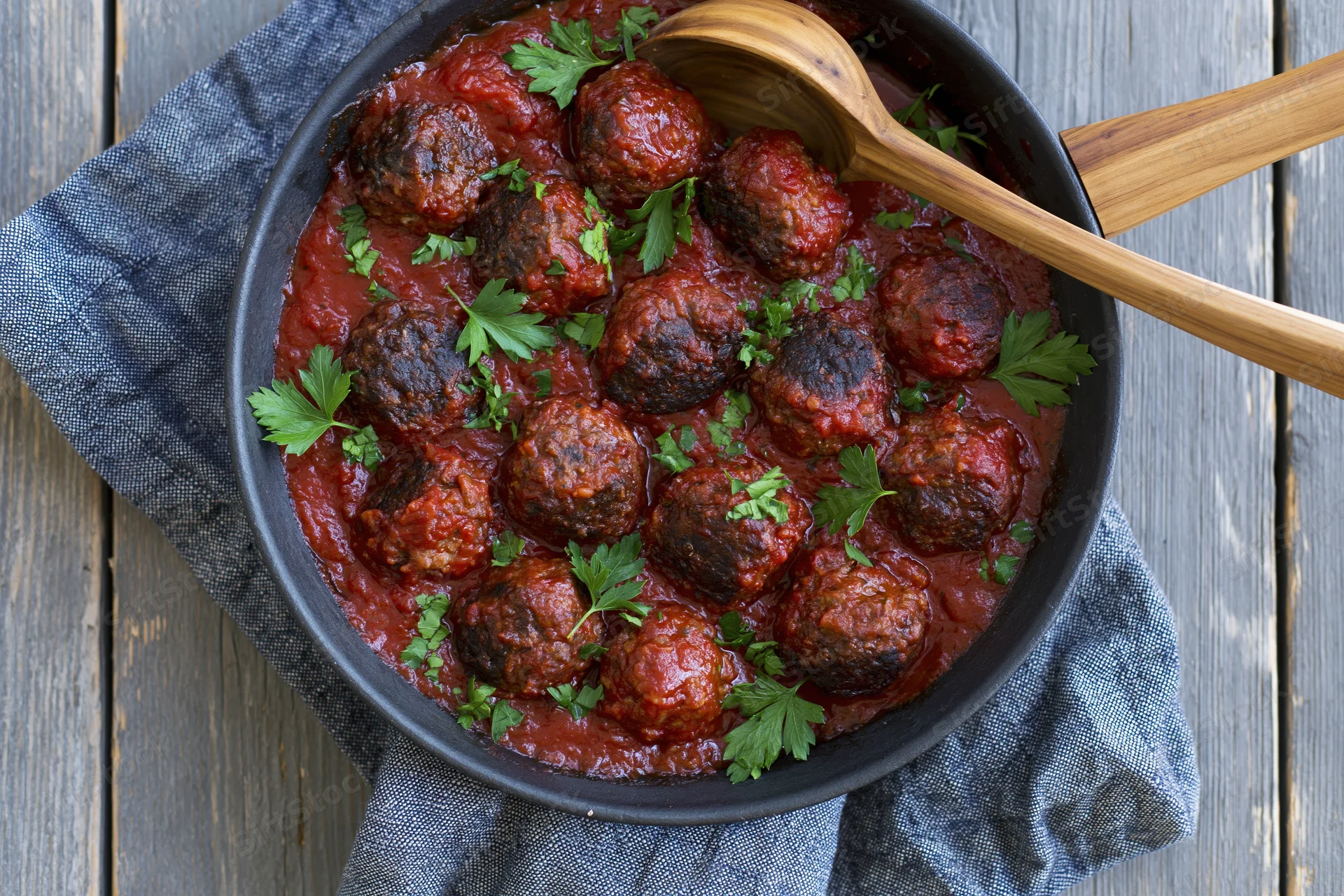 Meatballs in tomato sauce in a skillet with wooden spoon on a wooden table with gray cloth