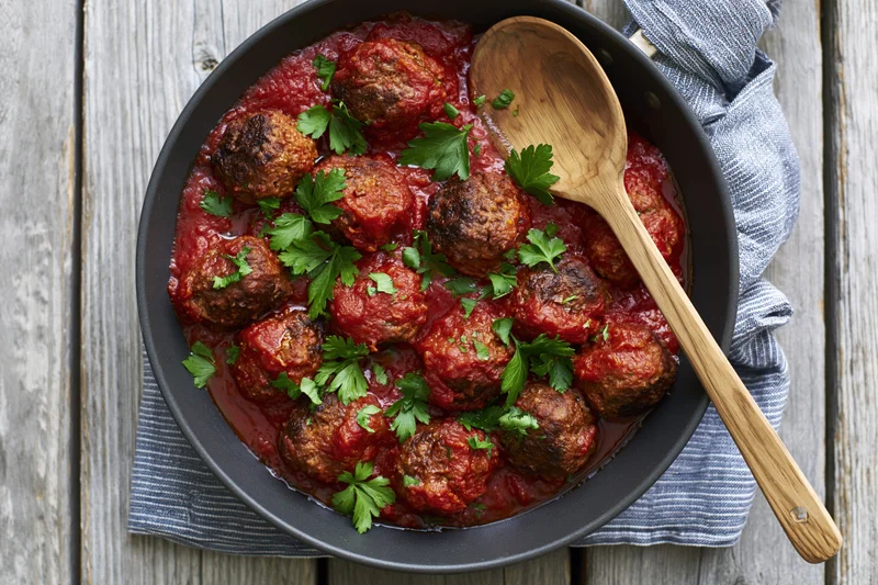 Meatballs in tomato sauce in a skillet with parsley garnish on a wooden table