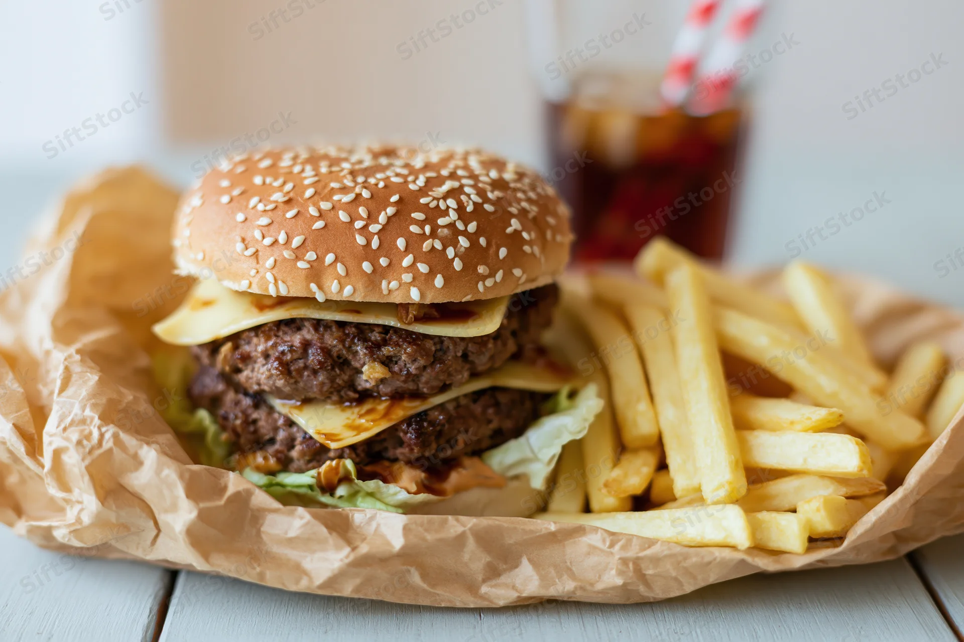 Double-stacked beef burger with cheese and sesame bun served with fries and soda on a paper-lined tray