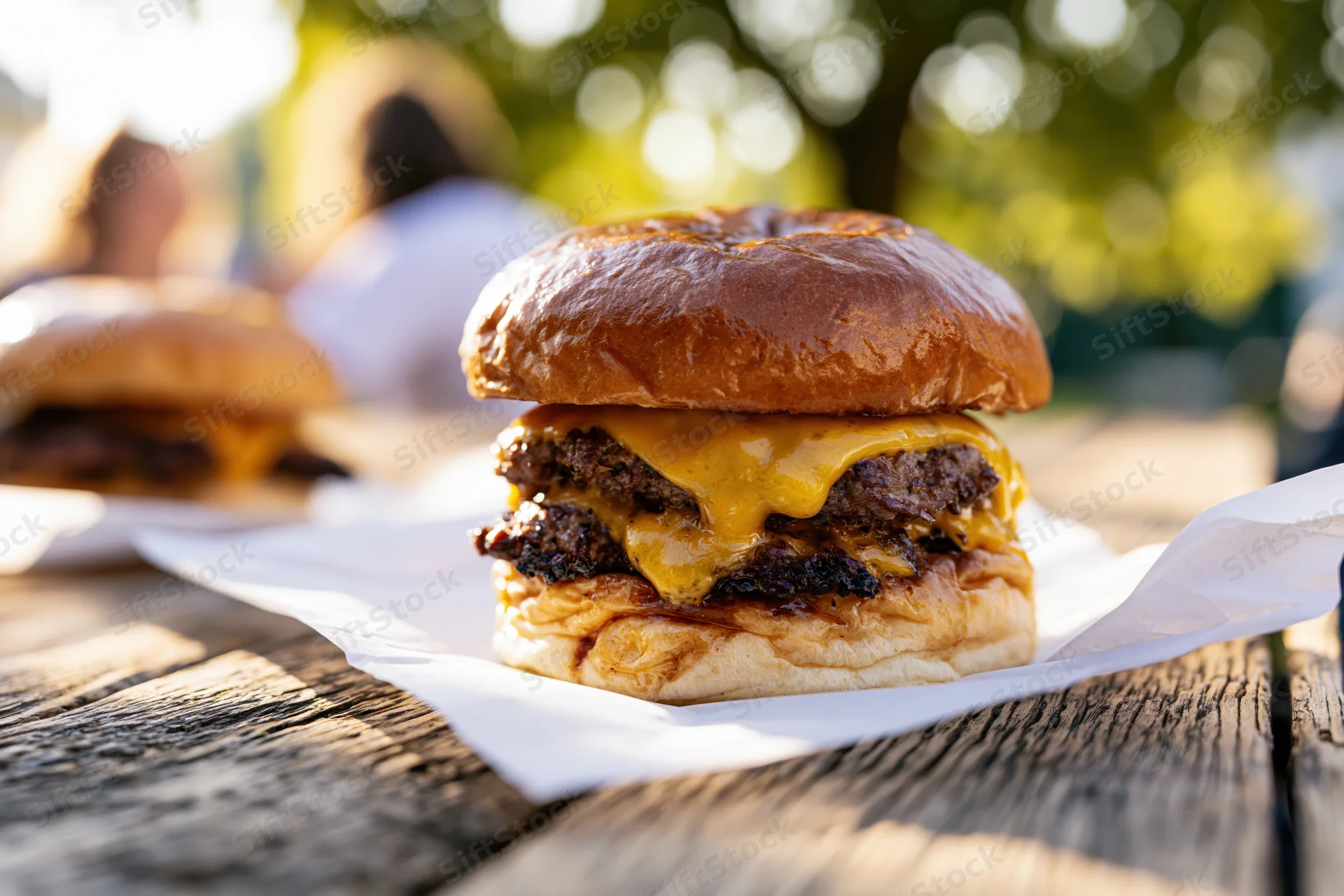 Double smash burger with melted american cheese oozing over grilled beef patties on a brioche bun on a wooden table outdoors