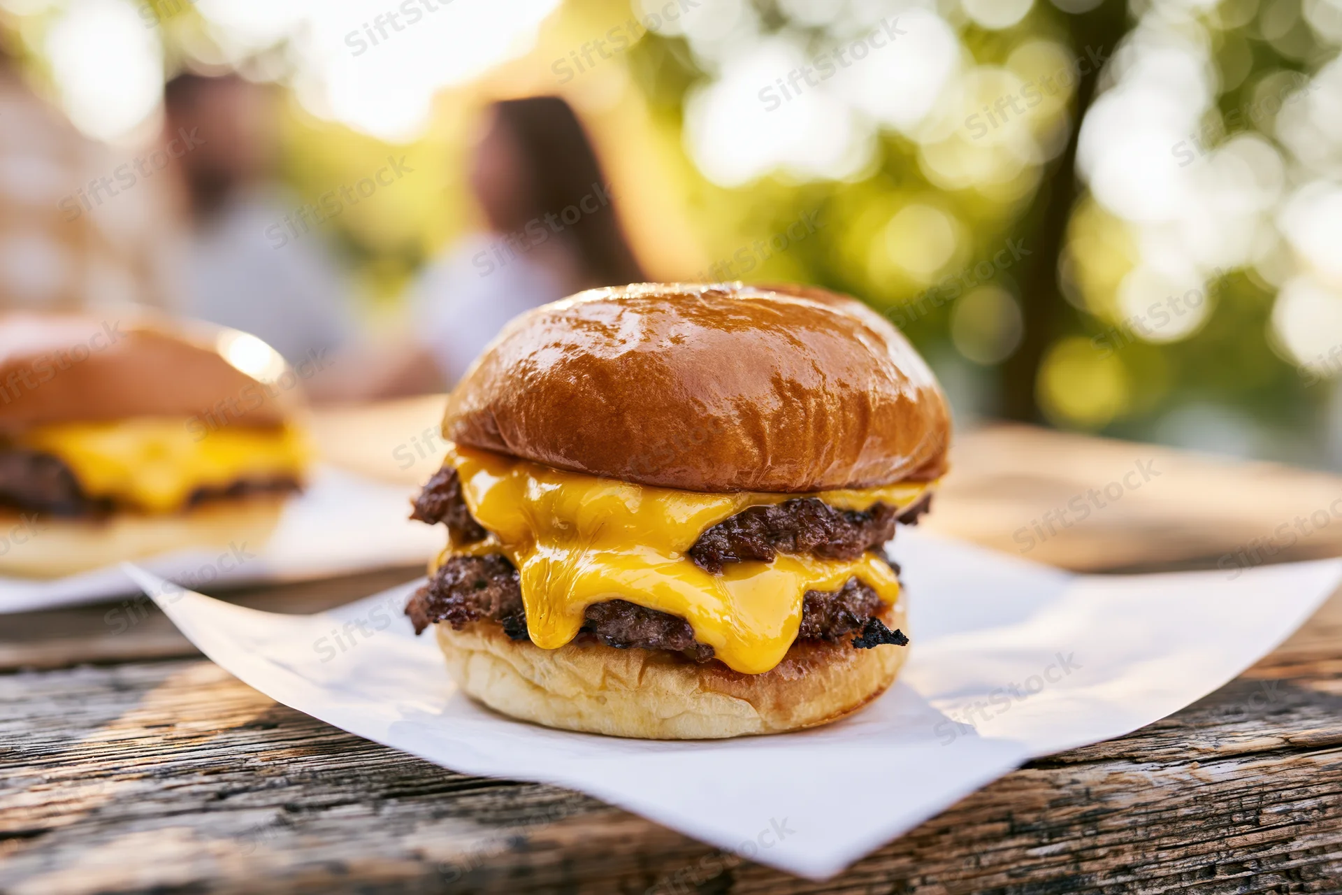 Double smash burger with melted american cheese oozing over beef patties on a wooden table outdoors