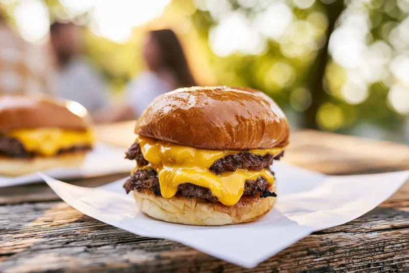 Double smash burger with melted american cheese oozing over beef patties on a wooden table outdoors