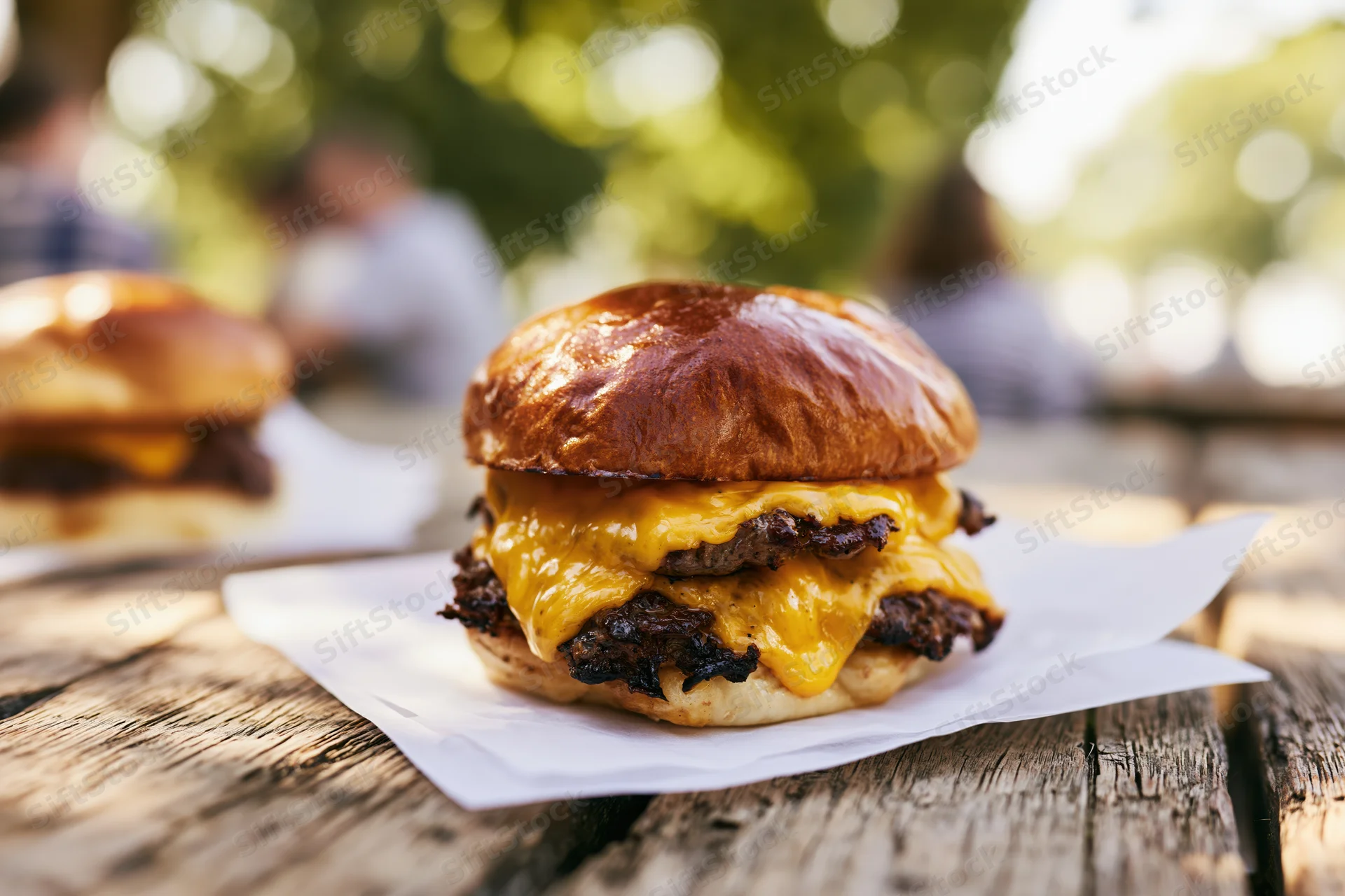 Double smash burger with melted american cheese on a wooden table outdoors