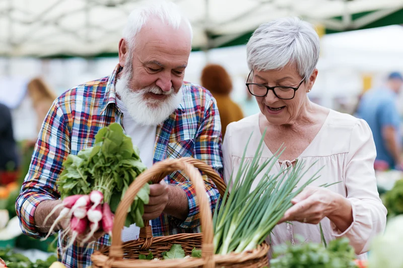 Senior couple smiling while selecting fresh vegetables at outdoor market stall