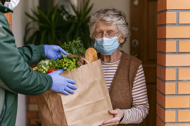 Elderly woman receiving groceries from a delivery person at her front door