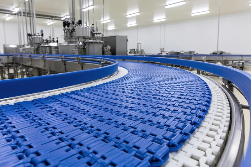 Blue modular plastic conveyor belt curving through industrial factory production area